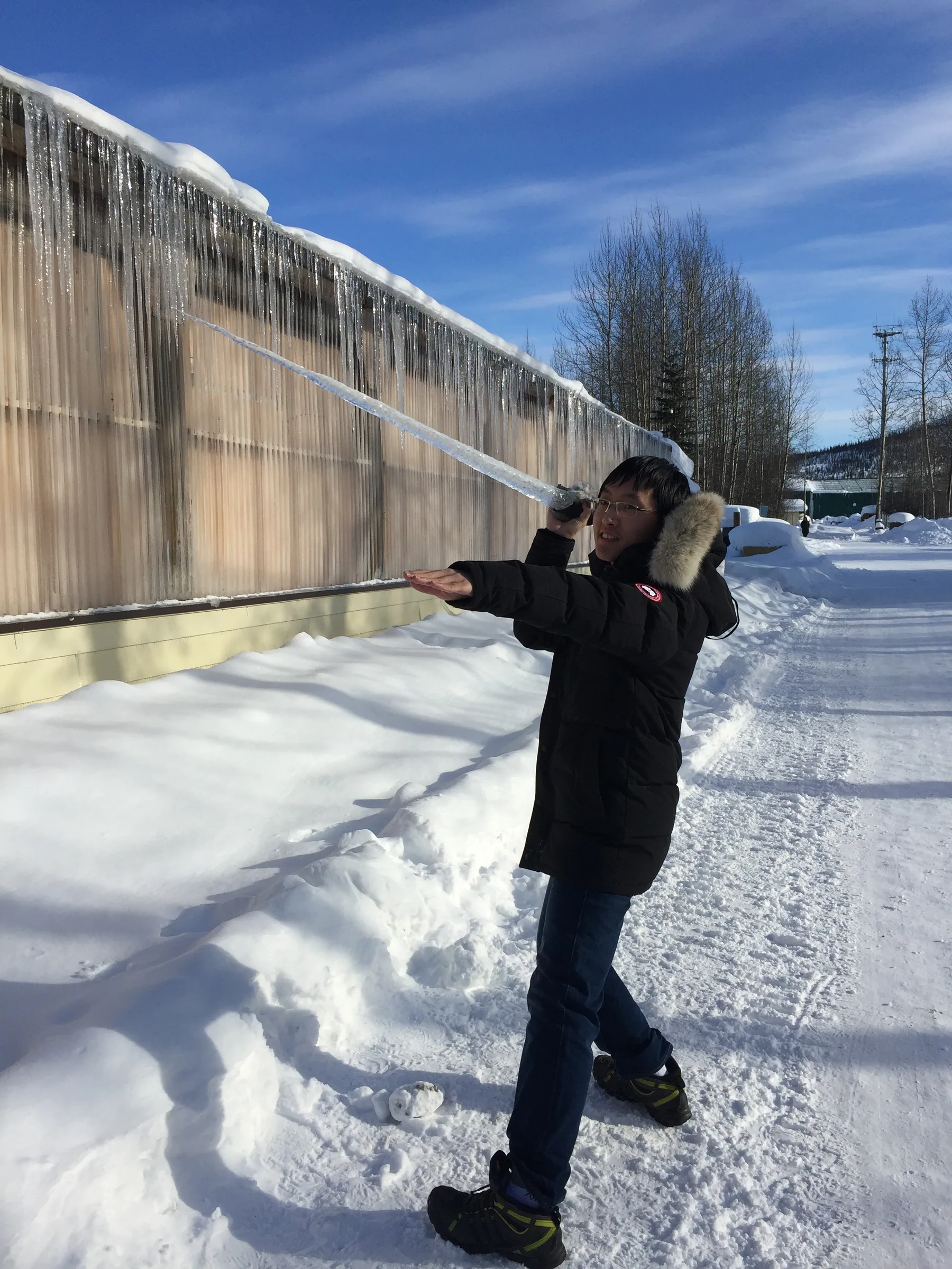 在积雪中的屋檐旁举着长冰柱留影